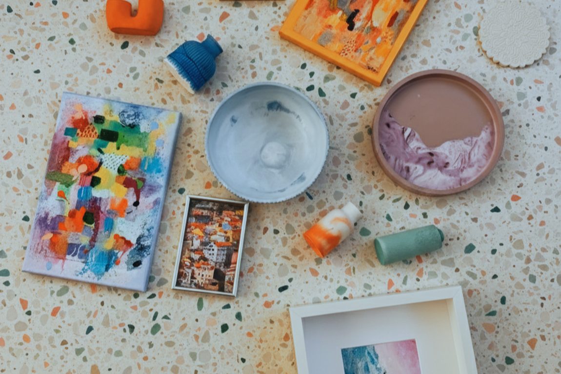 Mały obraz abstrakcyjny, oprawione prace i ceramiczne drobiazgi ułożone na posadzce z lastryko.